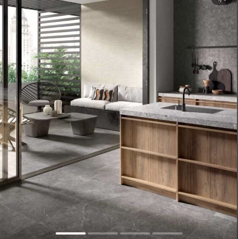 Open-concept living area with a marble-topped kitchen island, wooden cabinetry, gray stone floor, and a seating area by glass doors opening to a balcony.